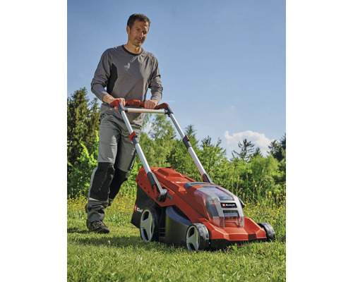 Muž tlačí červenou akumulátorovou sekačku na trávu na zahradě