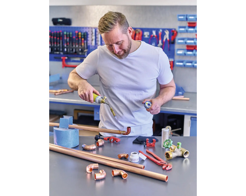 Muž pájí měděné trubky s plynovým hořákem v dílně.