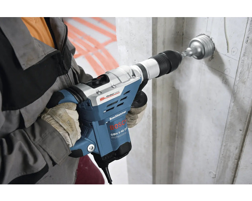 Muž vrtá otvory do betonové stěny pomocí vrtacího kladiva Bosch.