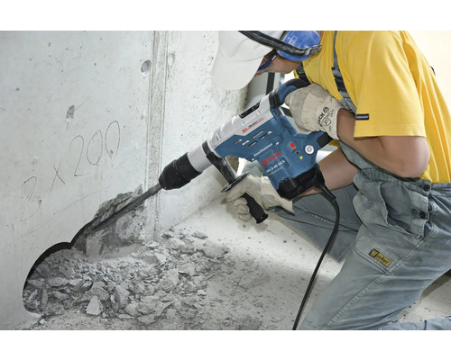 Dělník používá vrtací kladivo k vyvrtání otvoru do betonové zdi.