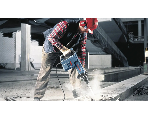 Dělník používá bourací kladivo na staveništi k rozbíjení betonu.