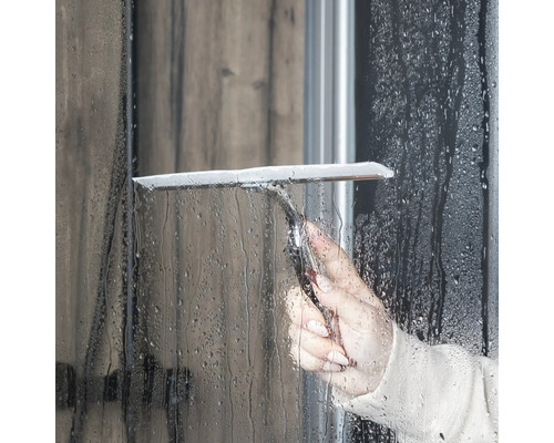 Osoba používá stěrku na sprchy k čištění sprchové stěny.