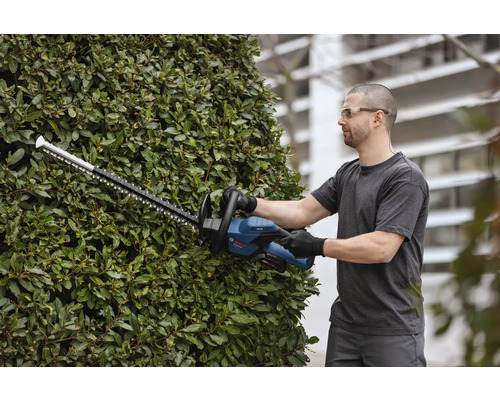 Muž stříhá živý plot pomocí akumulátorových nůžek na živý plot