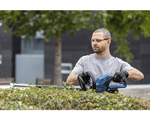 Muž stříhá živý plot nůžkami na živý plot od společnosti Bosch