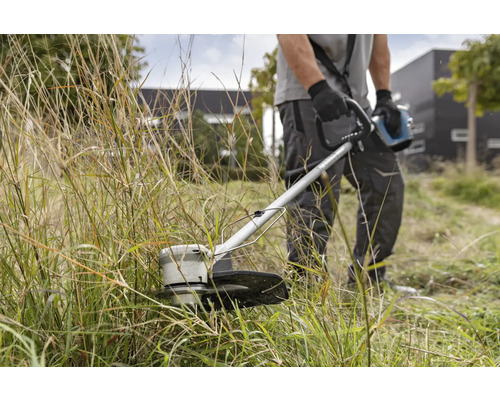 Muž stříhá trávu vyžínačem.