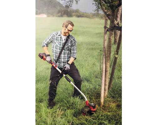 Muž stříhá trávu akumulátorovým vyžínačem na zahradě.