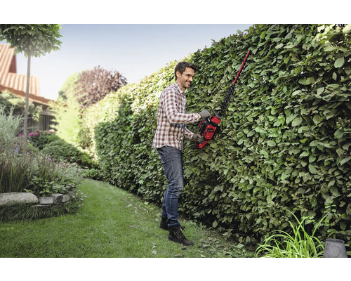 Muž stříhá živý plot v zahradě pomocí nůžek na živý plot.
