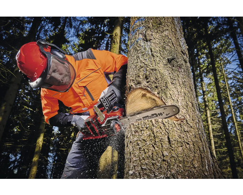 Muž v ochranném oděvu kácí strom motorovou pilou