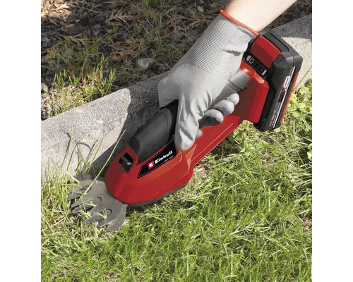 Osoba používá akumulátorové nůžky na trávu Einhell ke stříhání trávy podél okraje trávníku.