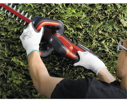 Osoba stříhá živý plot plotostřihem.