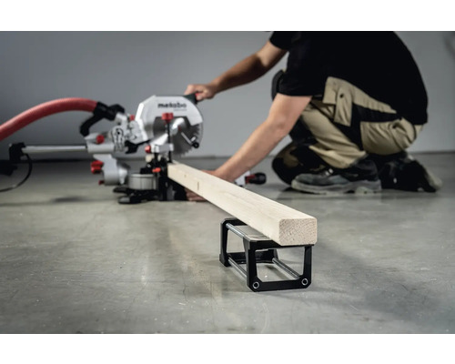 Osoba obsluhuje pokosovou pilu Metabo pro řezání kusu dřeva, který leží na podpěře obrobku.