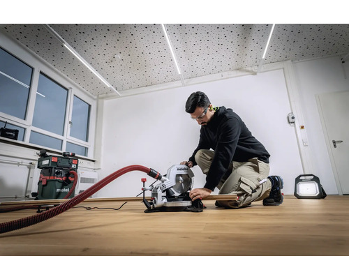 Muž pracuje s pokosovou pilou Metabo ve světlé místnosti. V pozadí je vidět vysavač a stavební světlo.