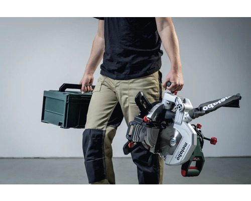 Osoba nese pokosovou pilu Metabo a kufrík na náradí.