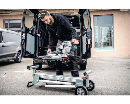 Muž s pokosovou pilou Metabo na pilovém stole před dodávkou