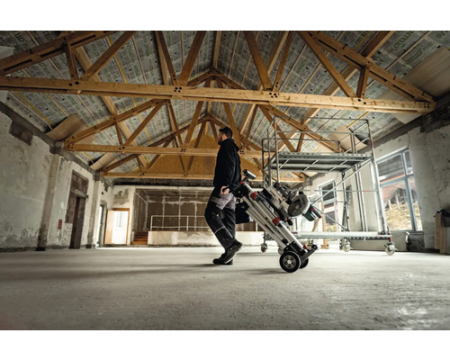 Muž přepravuje lešení na kolečkách v místnosti s dřevěnými trámy.