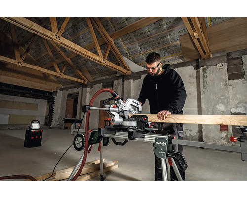 Muž pracuje s pokosovou pilou Metabo v hrubé stavbě na řezání dřevěné desky.