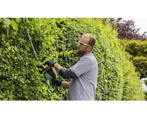 Muž stříhá živý plot nůžkami na živý plot.