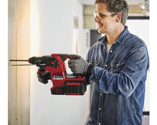 Muž vrtá díru do zdi pomocí akumulátorového vrtacího kladiva Einhell Herocco.