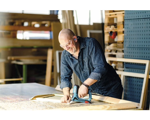 Řemeslník připevňuje látku elektrickou sešívačkou k dřevěnému rámu v dílně.