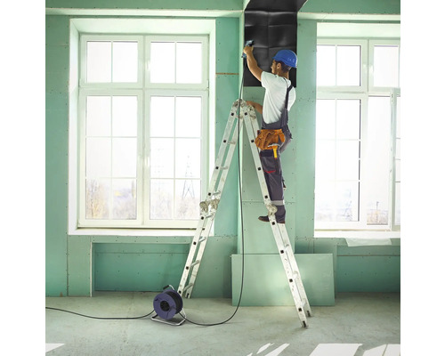 Řemeslník na žebříku připevňuje zvukově izolační desky ke stěně v místnosti.