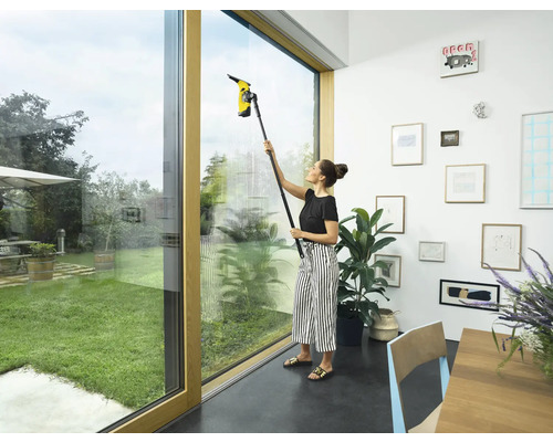 Žena čistí okna s okenním vysavačem v interiéru.