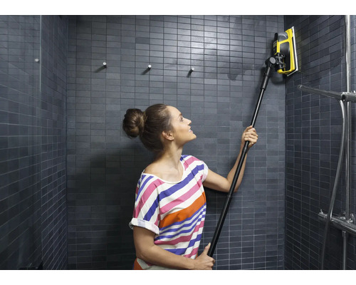 Žena čistí obkládanou sprchu stěrkou na okna s teleskopickou tyčí