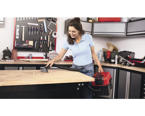 Žena čistí pracovní stůl mokrým a suchým vysavačem v dílně.