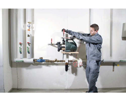 Instalace zahradního čerpadla řemeslníkem na stěnu s trubkami.