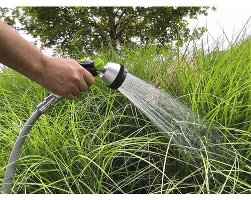 Ruka drží zahradní hadici, kterou se zavlažují zahradní rostliny.