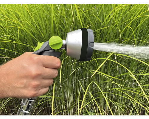 Ruka drží zahradní postřikovač, který stříká vodu.