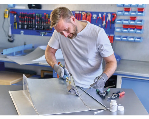 Řemeslník pájí kovové díly v dílně s nástroji a pracovním stolem