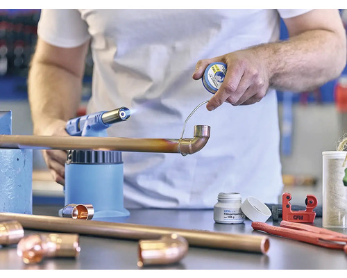 Řemeslník pájí měděnou trubku s pájecí lampou a pájkou