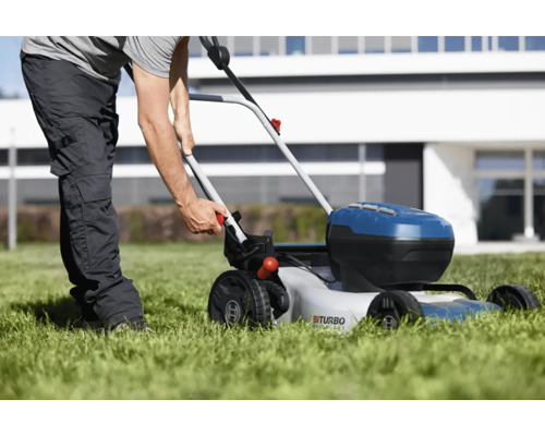 Osoba používá akumulátorovou sekačku na trávu na trávníku před domem.