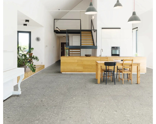 Světlý obývací pokoj s šedou dlažbou, kuchyňským stolem a schodištěm