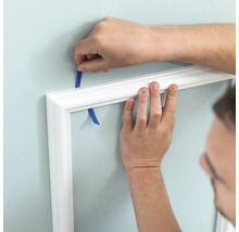 Připevnění bílé ozdobné lišty ke stěně pomocí lepicí pásky.