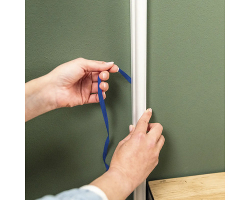 Ruce měří páskou vzdálenost k ozdobné liště