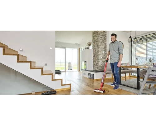 Muž čistí dřevěnou podlahu pomocí akumulátorového mopu s vysavačem v moderním obývacím pokoji