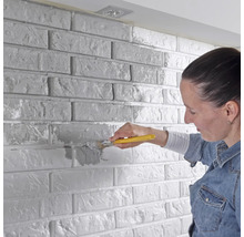 Žena natírá cihlovou zeď štětcem