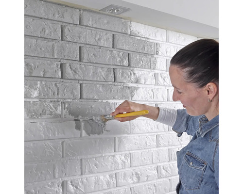 Žena natírá cihlovou zeď štětcem
