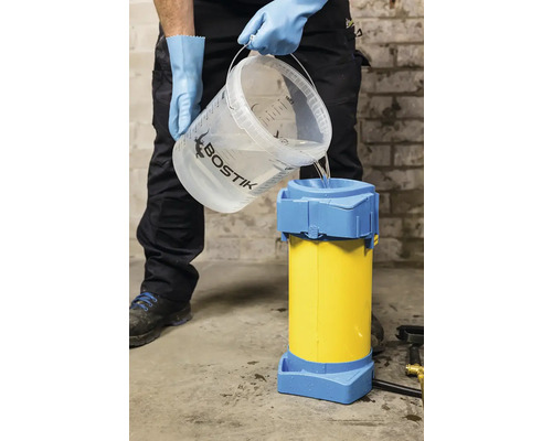 Osoba nalévá vodu z kbelíku s logem Bostik do míchačky na maltu.