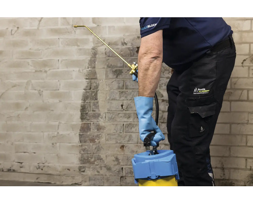 Osoba stříká stěnu rozprašovačem, aby ji ošetřila.