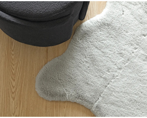 Detailní pohled na šedý koberec se vzhledem ovčí kůže vedle křesla na dřevěné podlaze