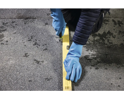 Osoba v rukavicích řeže nožem podél vodováhy na povrchu.