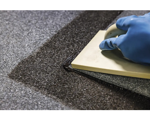 Ruka v rukavici a spárovací hladítko při spárování podlahových dlaždic