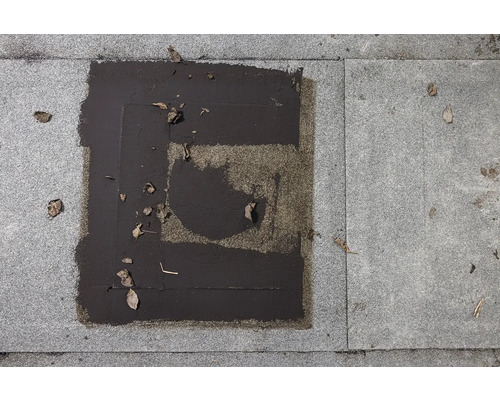 Detailní záběr dlažby s bitumenovými záplatami a listím