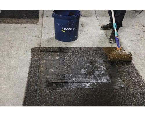 Aplikace střešní krytiny válečkem vedle kbelíku Bostik.