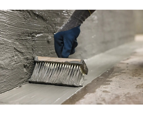 Osoba nanáší stěrkou těsnicí hmotu na stěnu a podlahu.