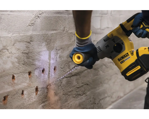 Osoba vrtá otvory do zdi pomocí vrtacího kladiva. Logo společnosti DeWalt.