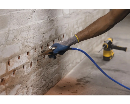 Osoba čistí vrtané otvory v cihlové zdi ofukovací pistolí v rámci přípravy na opravy.