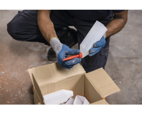 Osoba připevňuje červenou výlevku k prázdné láhvi nad kartonovou krabicí.